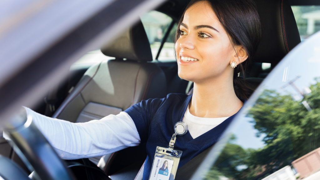 woman sitting in driver seat of car dressed in nurse attire with RN work badge.