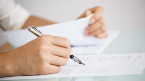 Person holding a pen filling out paperwork.